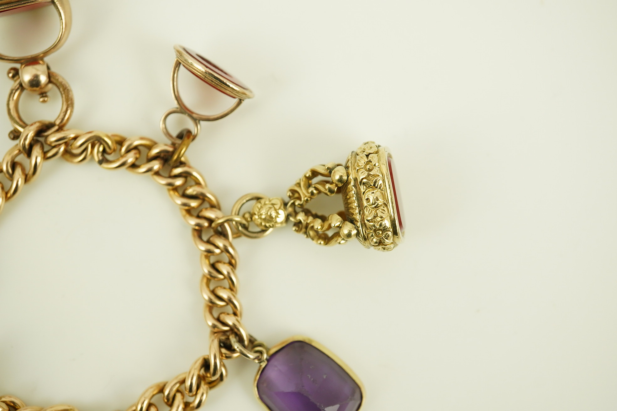 An Edwardian 15ct gold curb link charm bracelet with heart shaped padlock clasp, hung with six assorted gold overlaid and carnelian set fob seals